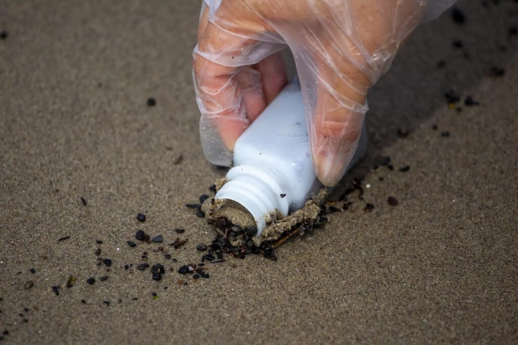 A hand in a clear glove collects a sand sample
