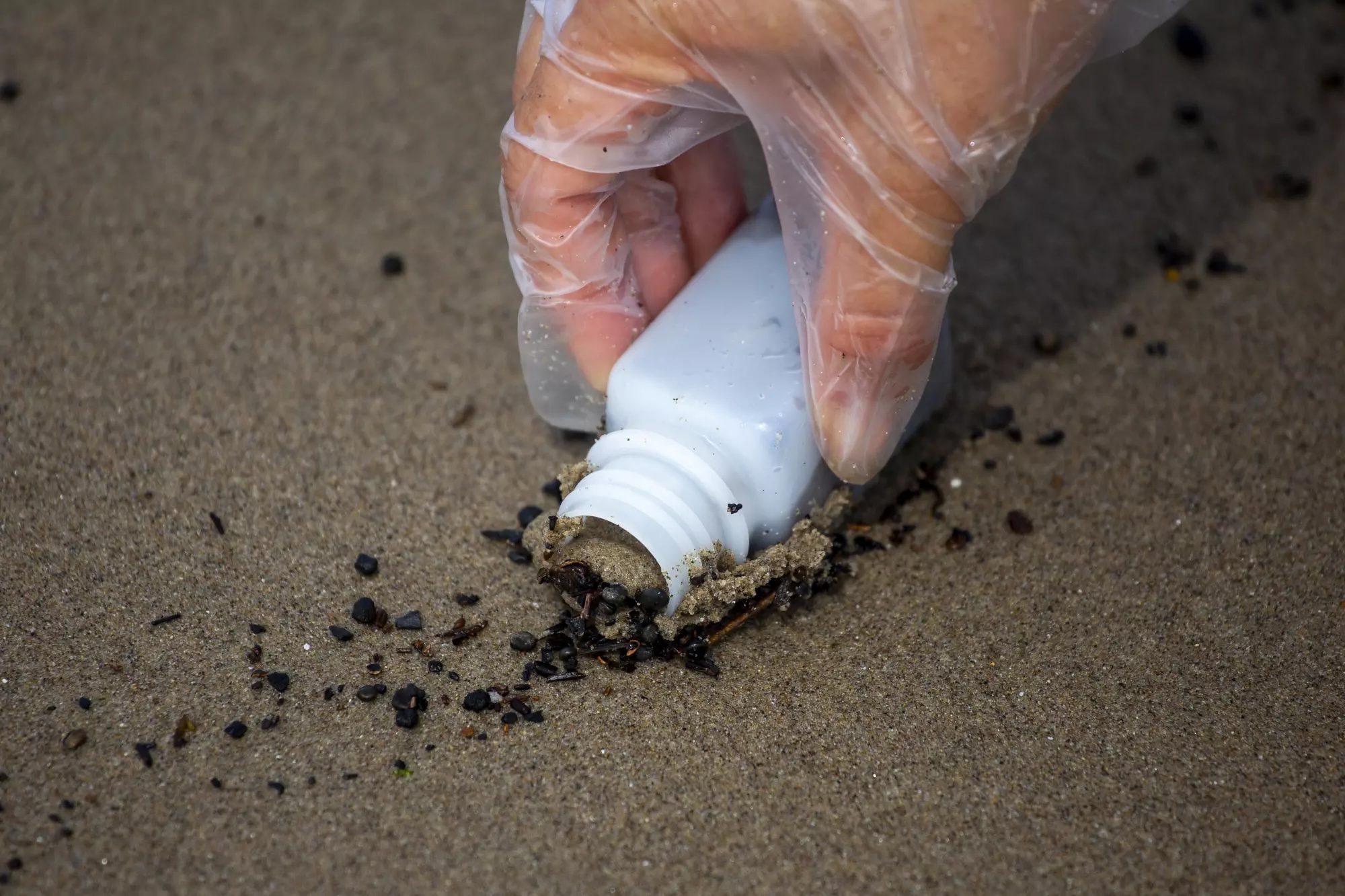 A hand in a clear glove collects a sand sample