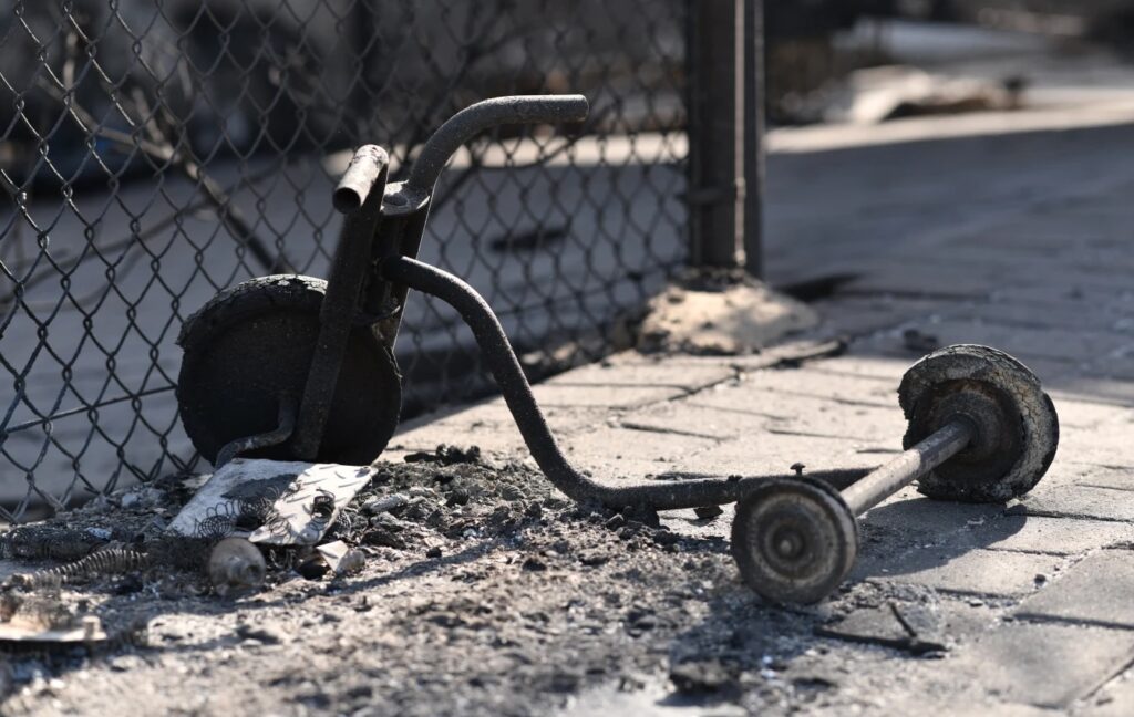THe image shows the frame a burnt tricycle next to a pile of ash, following a fire.